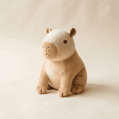 A cream and tan capybara plush toy photographed on a warm paper background